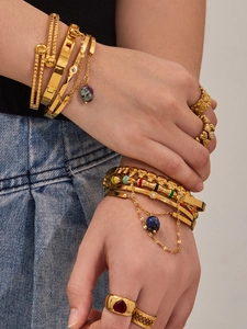 Détail de bracelets et bagues en acier doré sertis de pierres naturelles et de perles