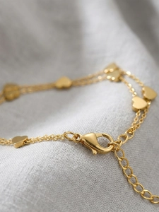 Macro detail of gold double-layered heart bracelet showing lobster clasp and link texture