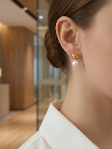 Détail de boucles d'oreilles cœur plaquées or 18 carats avec perles portées par modèle
