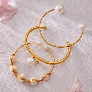 Set de pulseras abiertas bañadas en oro de 18k con perlas naturales sobre fondo de madera