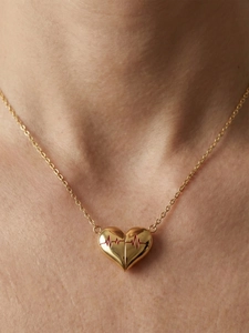 Macro del ciondolo a cuore dorato con linea ECG rossa su catena sottile dorata