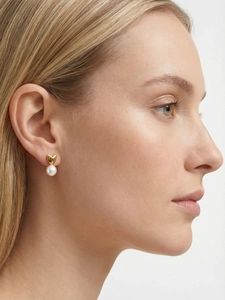 Gros plan d'une boucle d'oreille cœur dorée avec perle blanche portée par un mannequin