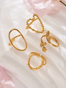 Detail of four gold geometric heart and flower rings on a white textured aesthetic stand