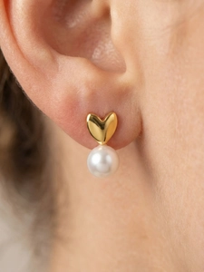 Détail macro d'une boucle d'oreille cœur dorée 18k avec une perle ronde blanche pendante
