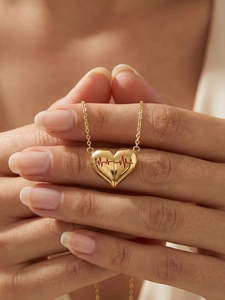 Dettaglio del ciondolo a cuore dorato con onda ECG rossa tenuto tra le mani