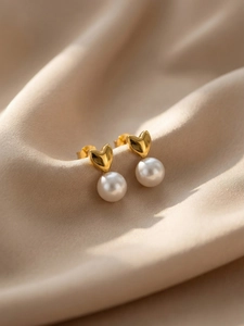 Vue macro des boucles d'oreilles cœur dorées 18k et perles sur fond de soie douce