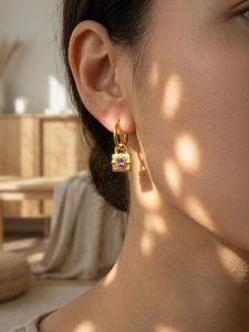 Gros plan de boucles d'oreilles cadenas dorées avec zircon violet portées par un mannequin