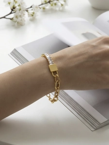 Detailopname van een gouden schakelarmband met rechthoekige zirkoon op de pols