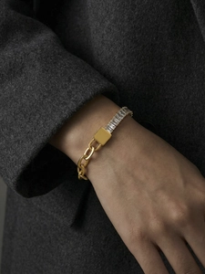 Detail van de gouden schakelarmband met ingelegde zirkoon en metalen merkplaatje