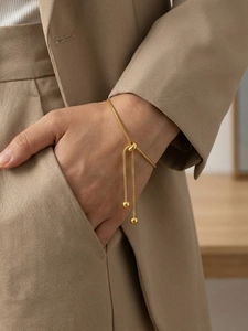Detail of adjustable gold snake chain bracelet with drawstring spheres on a khaki suit