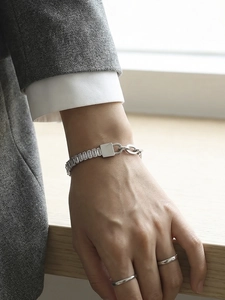 Detail van zilveren kettingarmband met rechthoekige zirkoon inleg en metalen plaatje