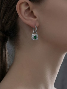 Détail de boucles d'oreilles cadenas argentées avec zircon vert sur mannequin