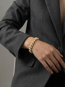 Détail du bracelet en acier doré avec perles blanches sur une veste de costume grise