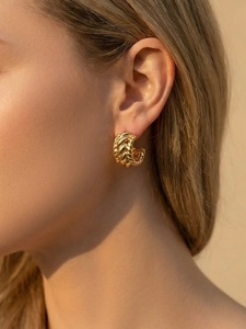 Détail de boucles d'oreilles créoles dorées torsadées avec texture tressée sur modèle