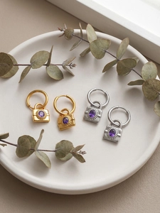Gros plan sur boucles d'oreilles créoles avec pendentif cadenas et pierre violette