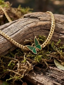 Macro detail of golden butterfly pendant with green enamel on mossy wood texture