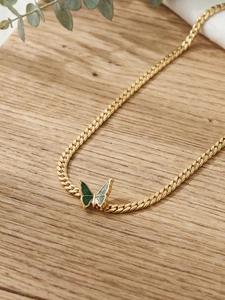 Detailed macro view of 18k gold plated Cuban chain with green butterfly pendant