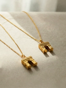 Close-up of 18k gold plated Arc de Triomphe pendants on textured fabric background