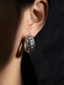 Vue latérale macro de boucles d'oreilles créoles C argentées portées sur modèle