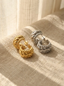Détail des boucles d'oreilles torsadées en C dorées et argentées sur un tissu en lin