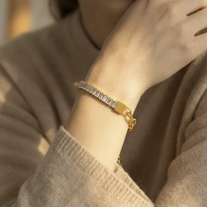 Elegante gouden kettingarmband met rechthoekige zirkoonstenen op een gebreide trui