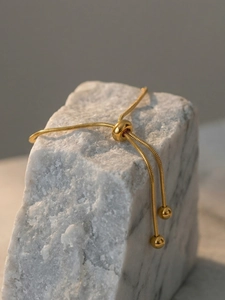 Macro detail of adjustable sliding buckle on golden snake chain bracelet with ball ends