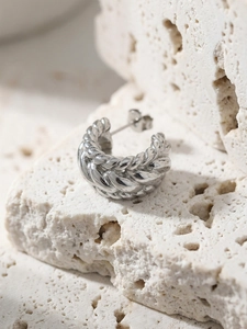 Détail macro de boucles d'oreilles créoles torsadées argentées sur pierre de travertin
