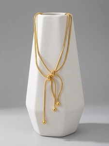 Detail of adjustable gold snake chain necklace with spherical beads on white ceramic vase