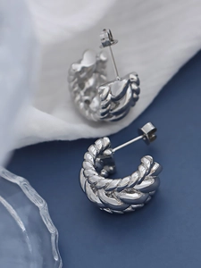 Détail de boucles d'oreilles créoles torsadées argentées sur tissu bleu élégant