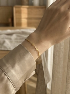 Detail of a minimalist gold cross charm bracelet on a female wrist with silk sleeve