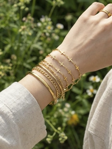 Close-up of layered gold cross pendant bracelets and sleek bangle on wrist