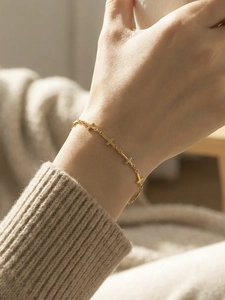 Close-up of gold chain bracelet with multiple small cross charms worn with cozy knitwear