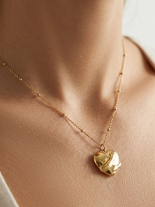 Close-up of gold-plated 3D heart pendant and beaded chain necklace on model