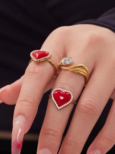 Détail de bagues cœur rouge avec halo de zircons et bague plume dorée sur la main