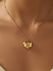 Macro detail of a 3D gold-plated heart pendant on a delicate beaded chain necklace
