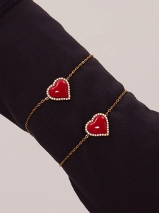 Détail de bracelets en chaîne dorée avec pendentifs cœur rouge et bordure en zircon
