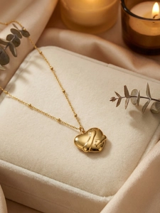 Detailed view of a gold hugging heart pendant on a beaded chain over elegant silk
