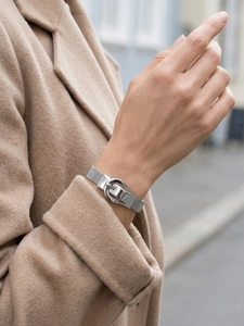 Close-up of silver mesh bracelet with horseshoe buckle on woman wearing camel coat