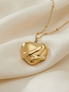 Macro view of gold plated hug heart pendant with bead chain on white silk background