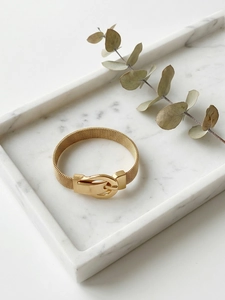 Detailed close-up of golden mesh bracelet with buckle on white marble tray
