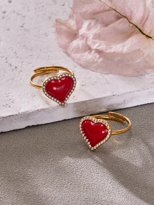 Détail de bagues dorées avec cœurs en émail rouge et zircons dans un décor élégant