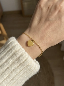 Detailed close-up of a delicate gold heart pendant bracelet worn on a female wrist
