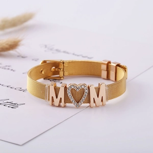 Close-up of golden mesh bracelet with MOM lettering and a heart-shaped zircon stone