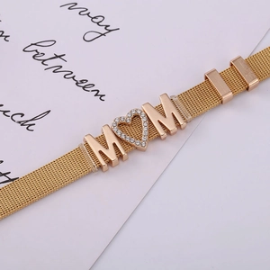 Detail of golden mesh bracelet featuring MOM lettering and heart-shaped rhinestone inlay