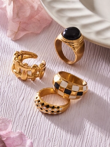 Close-up of four gold-plated stainless steel rings with black and white enamel patterns