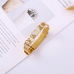Gold mesh bracelet with diamond butterfly, heart, and tiny angel pendant on magazine