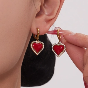 Boucles d'oreilles dorées avec cœurs rouges et bordure en zircon portées à l'oreille