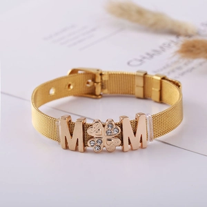 Gold mesh band bracelet with MOM and clover charms on a magazine background