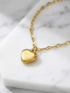 Close-up of a polished gold heart pendant with mirror finish on marble tile