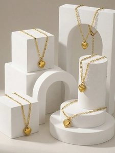 Polished gold-tone heart pendants on flat chains displayed on geometric blocks